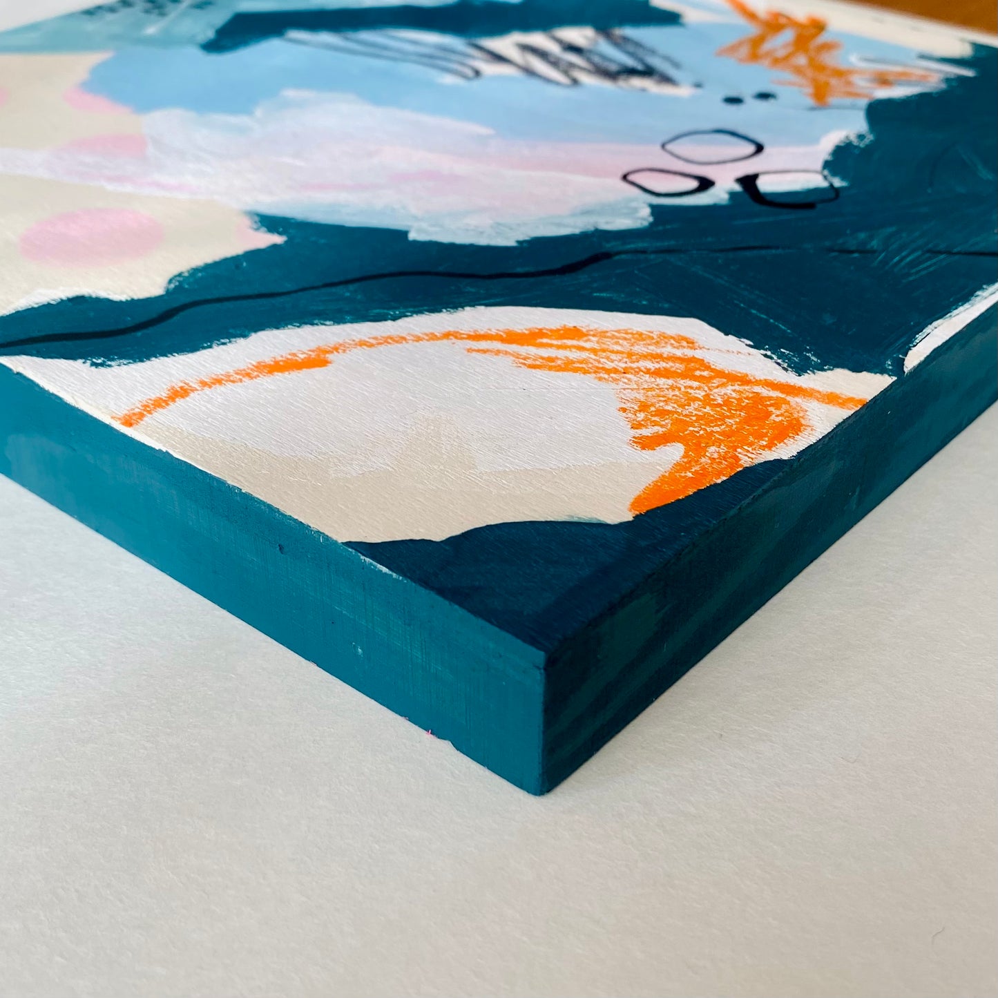 Close-up of a colorful abstract painting with a blue frame on a light gray surface.