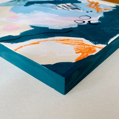 Close-up of a colorful abstract painting with a blue frame on a light gray surface.